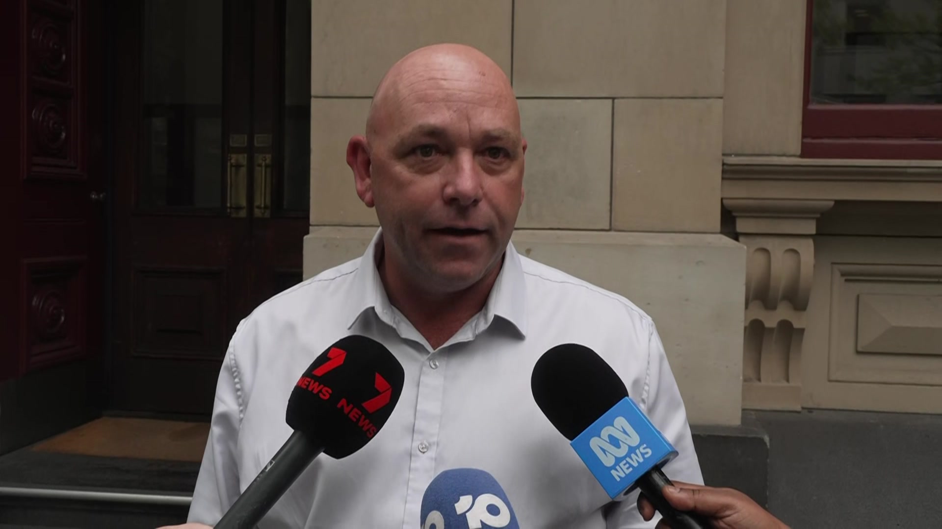 Richard habla con varios micrófonos sostenidos por reporteros, el Canal 7, los logotipos de ABC a la vista.