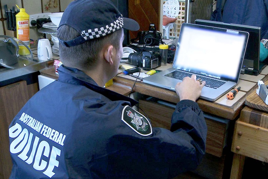 An Australian Federal Police officer looks at the contents of a seized laptop