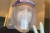 Katy Gallagher wears PPE mask and gloves, and does a peace sign to the camera in a house. 