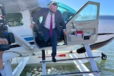a man in a suit gets out of a sea plane on the water
