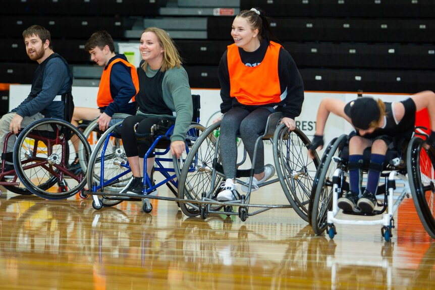 a number of wheelchair basketballer accelerate after the ball, all smiles
