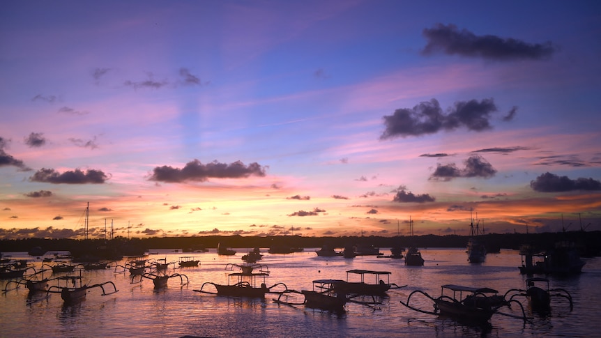 Boats drift in a small port at sunset in Bali.
