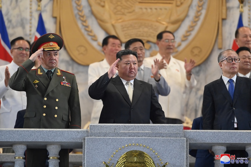 Kim Jong Un and Russian military general salute on a podium 