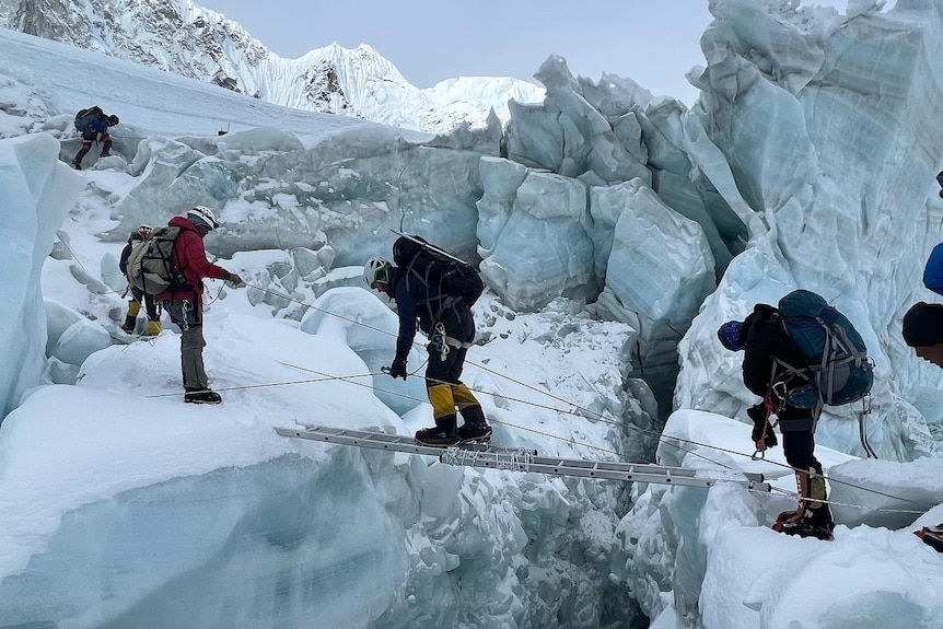 Climbers cross over a crevasse in the Himlayas, inching along a ladder.
