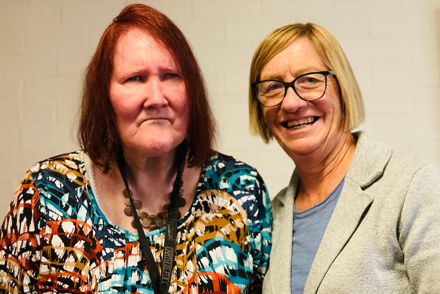 Two women smile for a photo together. One on the left has red hair and the one on the right has blonde hair