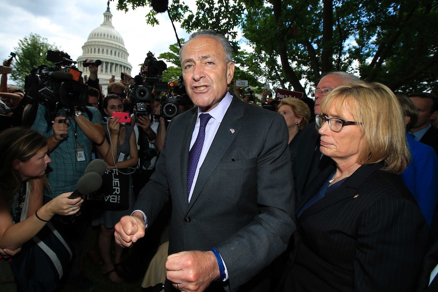 Senate Minority Leader Chuck Schumer stands with clenched fists outside the Capitol in Washington, surrounded by a media pack.