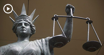 Scales of justice statue. White play button superimposed.
