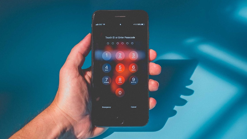 A man holds a smart phone, locked on the touch ID and passcode screen.