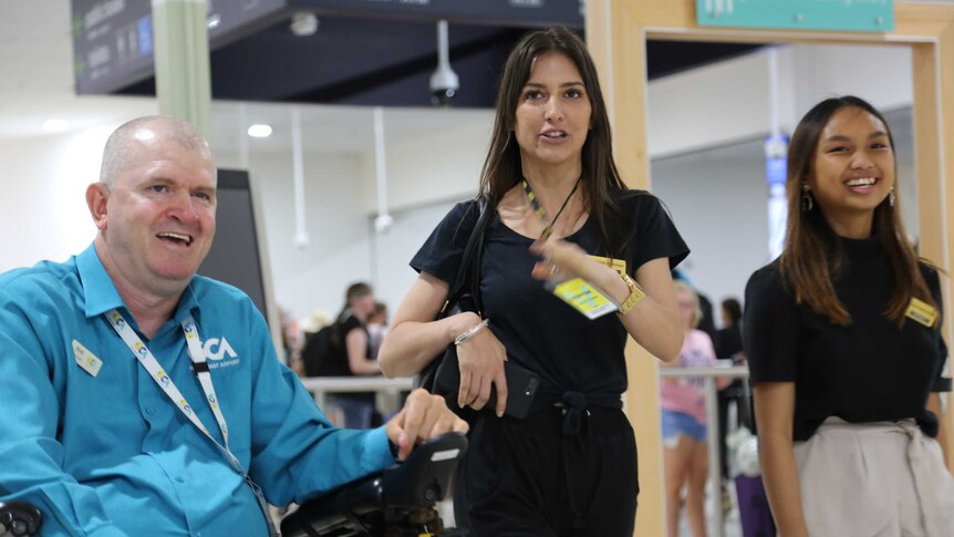 Brett Morris sits in a wheelchair next to two women at Gold Coast airport.