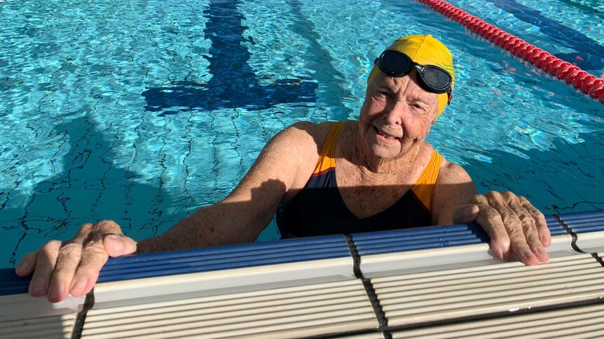 Nita McAuley has a swimming cap on and goggles. She is at the start of the lane in a pool.
