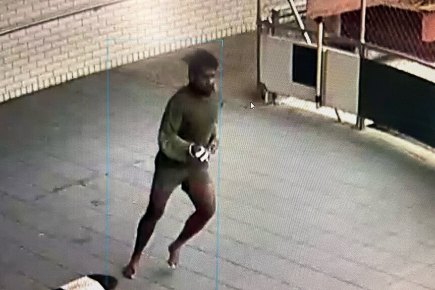 CCTV still shot of a man in a green long-sleeve shirt running in an undercover space