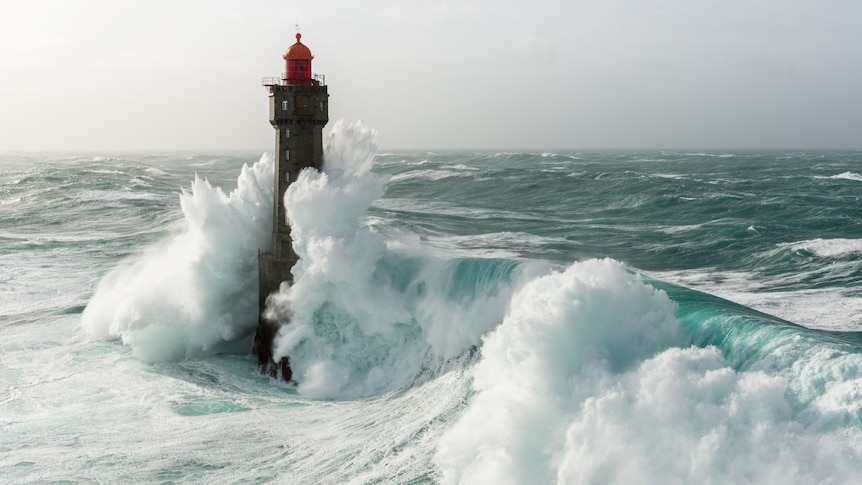 A lighthouse with waves crashing over it.