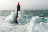 A lighthouse with waves crashing over it.