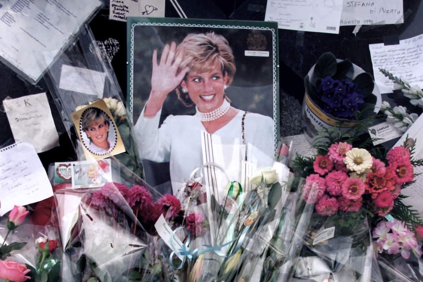 Flowers, photographs, candles and cards are piled up around a photo of Princess Diana.