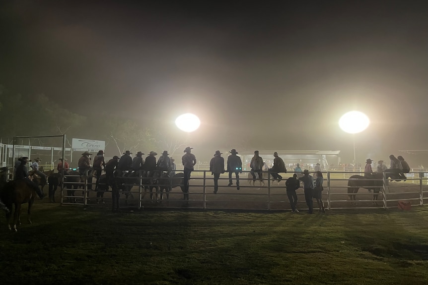 People sit on a fence at a rodeo.