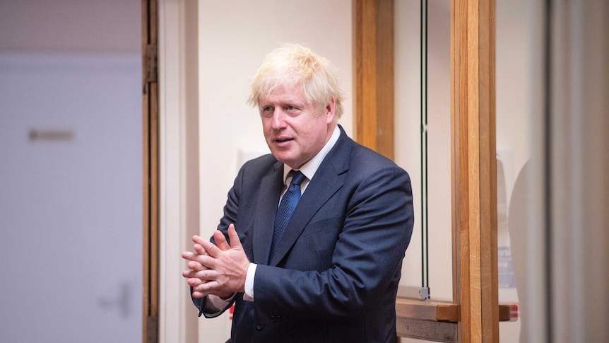 A man in a blue suit rubs his hands together