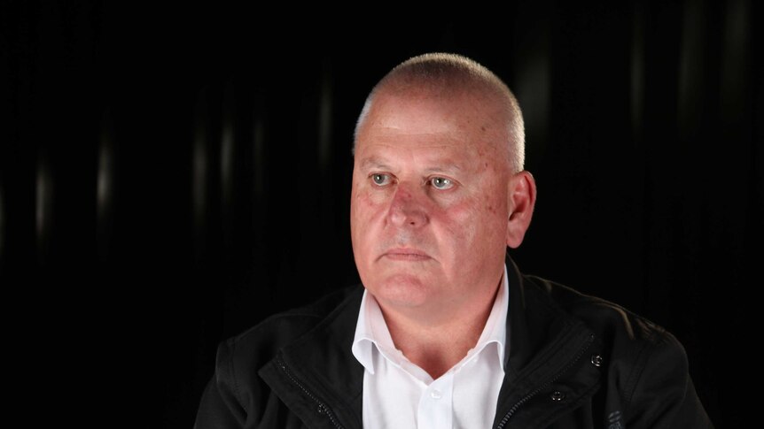 Pat Allen sits in a black jacket in front of a black background