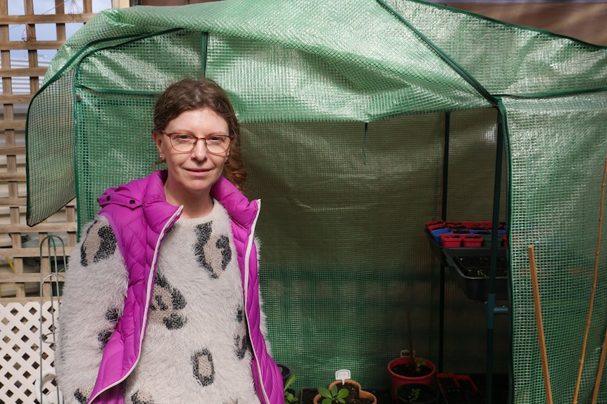 A lady standing in front of a greenhouse.