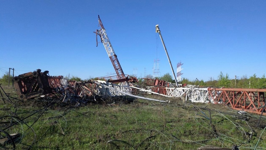 A radio tower made of white and red metal lies twisted on the ground, some of it blackened
