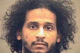 A police mug head shot of a young Middle Eastern man with curly black hair and black beard 
