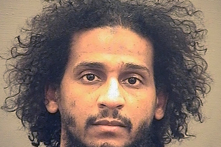 A police mug head shot of a young Middle Eastern man with curly black hair and black beard 