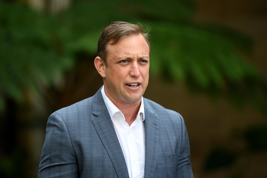 Blonde man in grey suit jacket, white shirt looks ahead