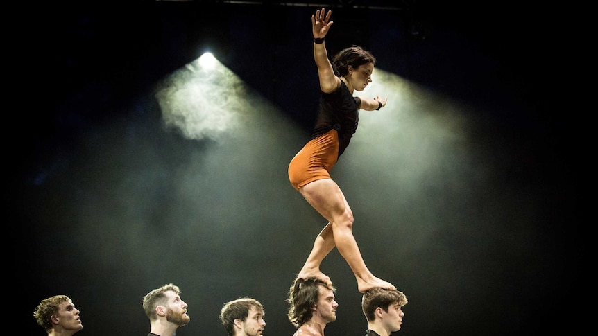Circus company Circa performing on stage, a woman acrobat balancing on the heads of men