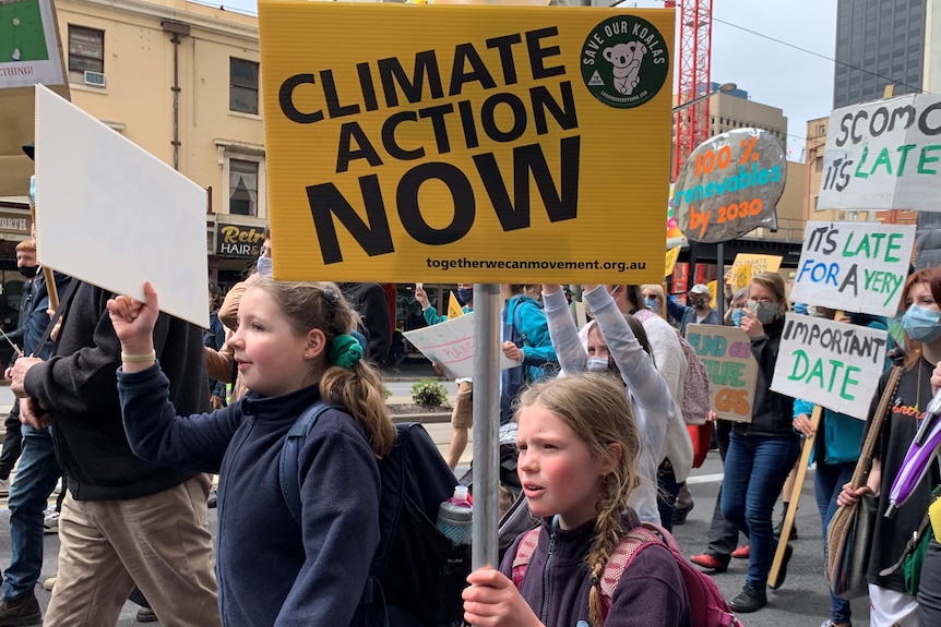 A crowd of protesters hold signs demanding climate action
