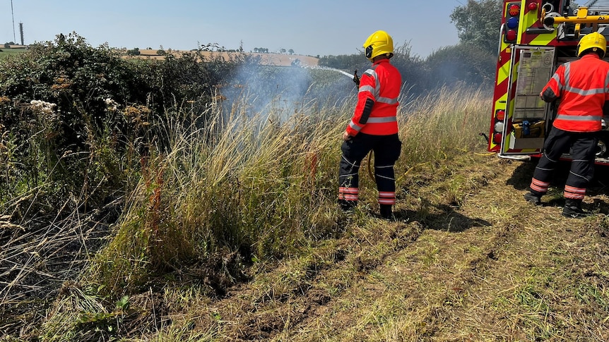 a firefighter dressed in red with yellow helmet holds a hose in a paddock