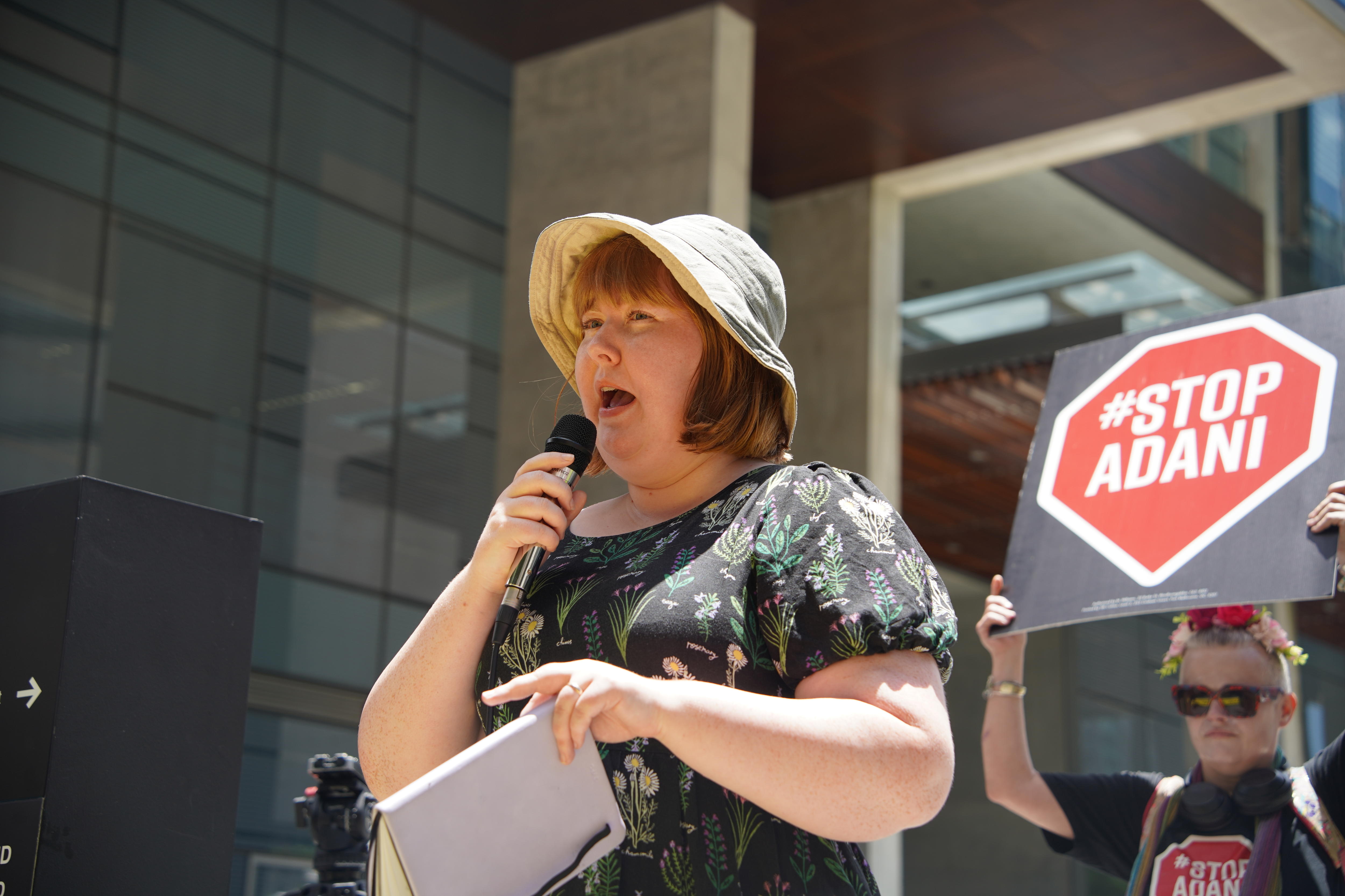 A woman holding a microphone, addressing a crowd of protestors.