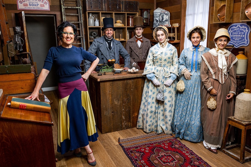 A woman standing next to a family dress in period costume in an old shop.