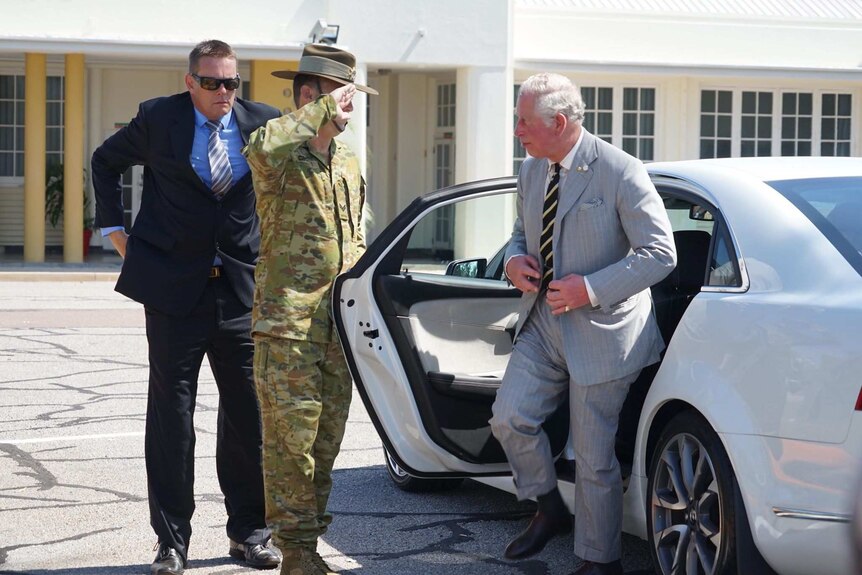 Prince Charles steps out of a car and is saluted by a soldier