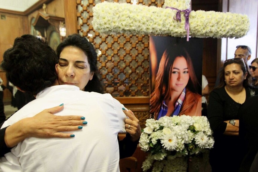 Relatives hug as a portrait and flowers of air hostess killed in air crash sit in background
