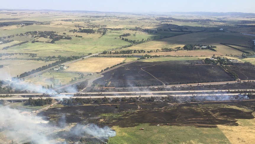 Smoke rises from blackened grass on either side of the Hume Highway.