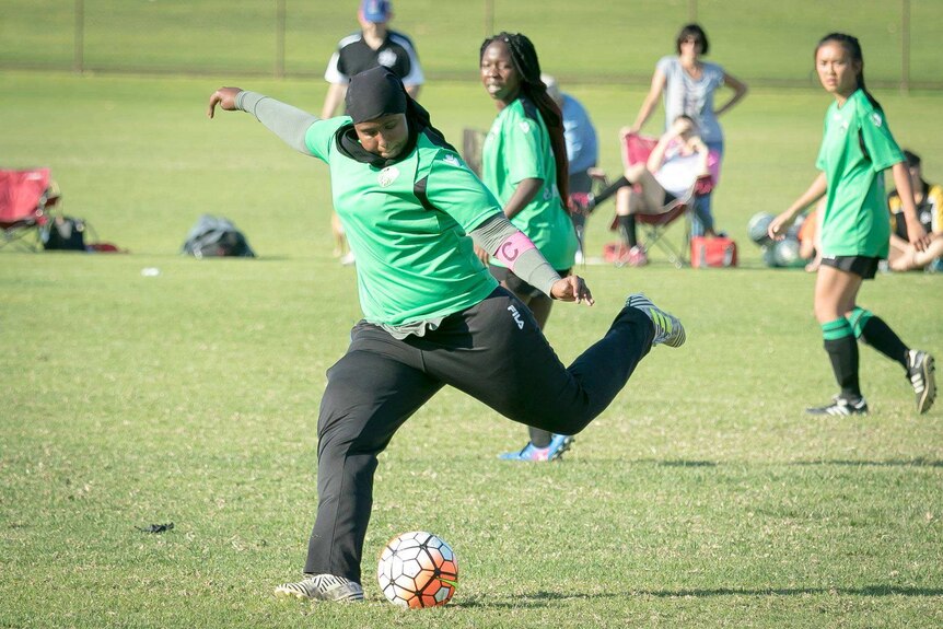 A girl playing for Balga Soccer Club winds up to kick a soccer ball as two teammates look on.
