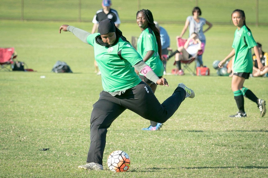 A girl playing for Balga Soccer Club winds up to kick a soccer ball as two teammates look on.