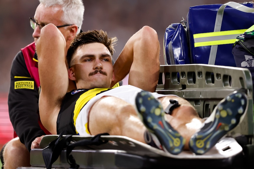 Josh Gibcus holds his head as he is stretchered off