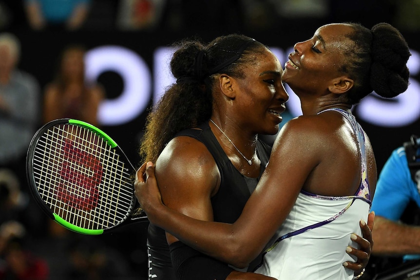 Venus and Serena hugging and smiling, one holding a racquet