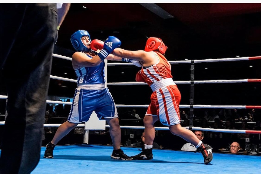 Two boxers fight in the middle of the ring. Tameika Garcia is wearing a red helmet and is throwing a left hand punch.