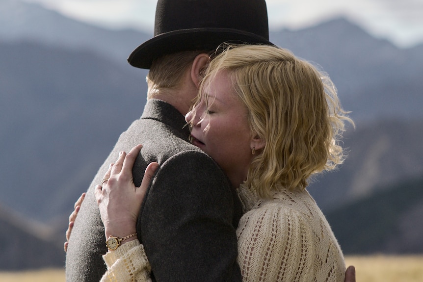 A 30-something woman cries while clutching a 30-something man wearing a bowler hat