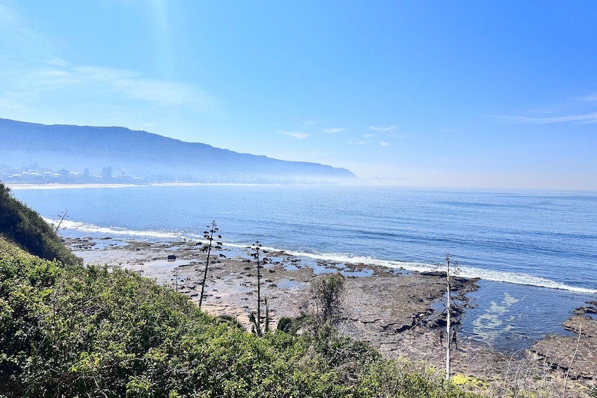 Hazy smoke lingering above the water as the view looks out from a beach with a mountain in the background