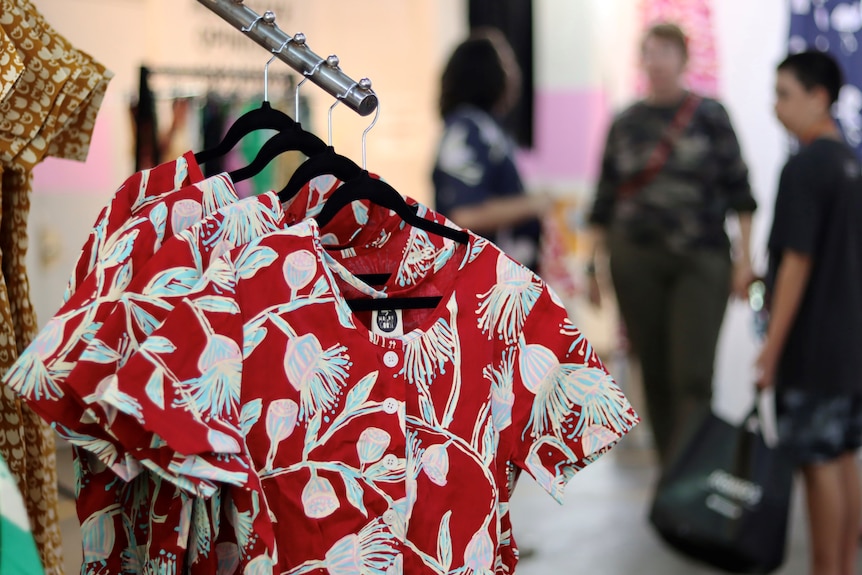 Red dresses with white and blue flowers on them hang on a rack.