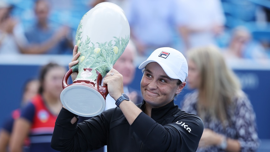 Ash Barty holds a large white trophy and smiles