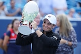 Ash Barty holds a large white trophy and smiles