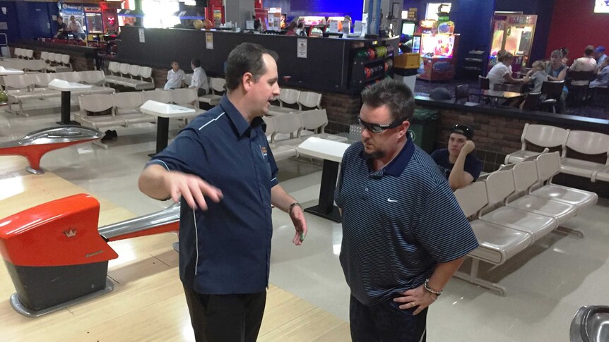 Two men at a bowling alley, one explaining something to another