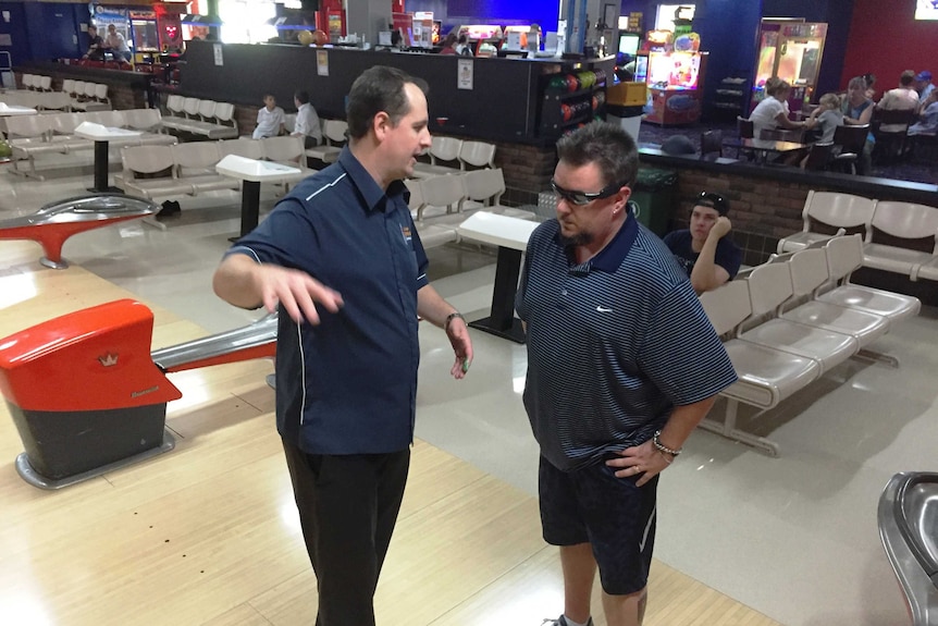 Two men at a bowling alley, one explaining something to another