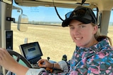 A teenage girl smiling as she sits in a tractor cab.