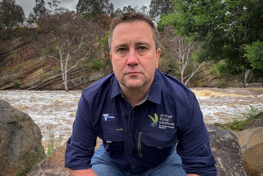 Man wearing navy shirt sitting on a rock.