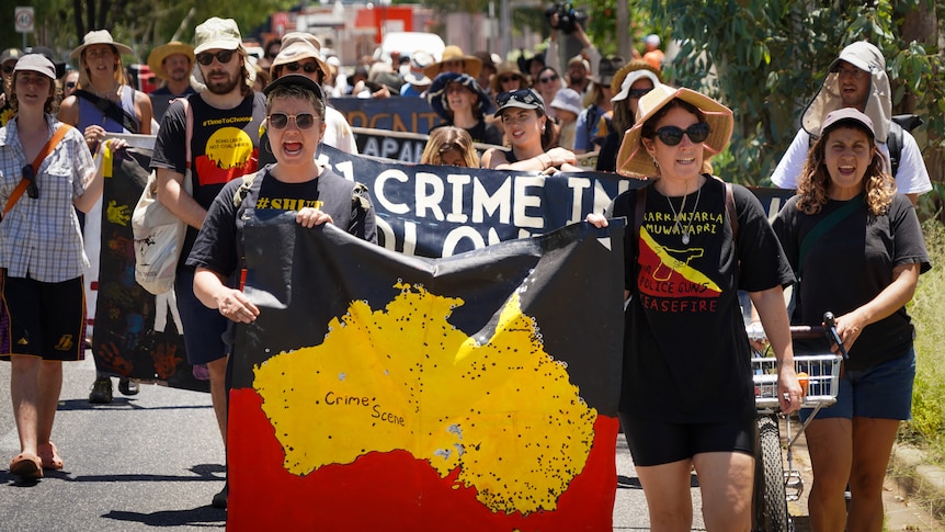 Protesters in indigenous flag colours march along a street holding flags and shirts protesting Australia Day