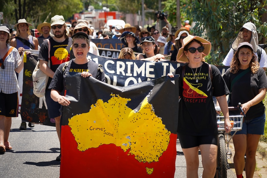 Protesters in indigenous flag colours march along a street holding flags and shirts protesting Australia Day